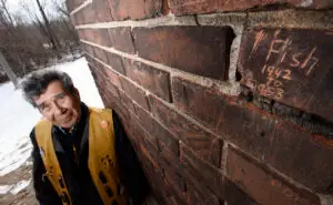 Geronimo, a Mohawk Institute Survivor, stands where as a young man he carved his nickname ‘Fish’ and the years he attended the school ( 1942–1953), into the bricks of the Mohawk Institute. Photo Cred: Hamilton Spectator